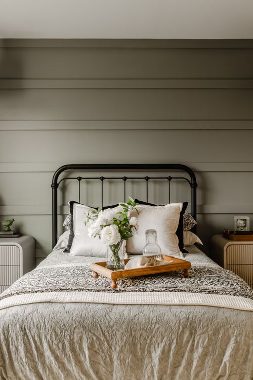 Bedroom with a black iron bed, fresh peonies on a tray and a shiplap accent wall