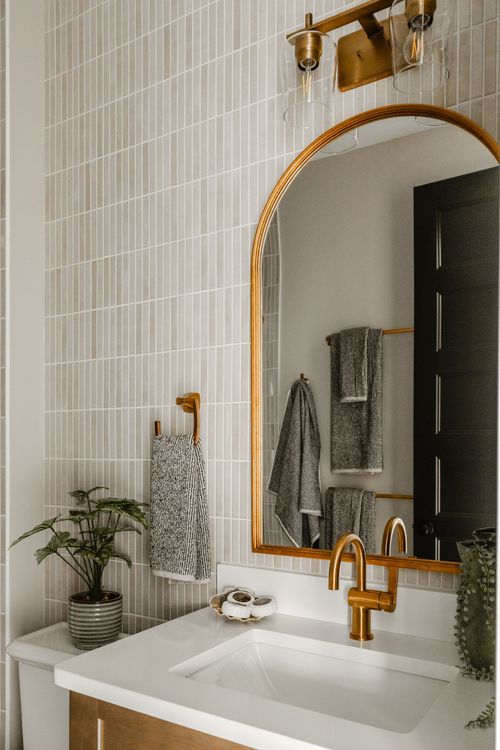 Bathroom vanity with an arched brass mirror, brass sconce and patterned tile wall