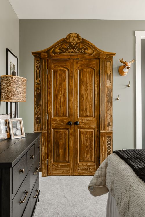 Ornate carved wood armoire with a lion crest, doors closed, beside a black dresser