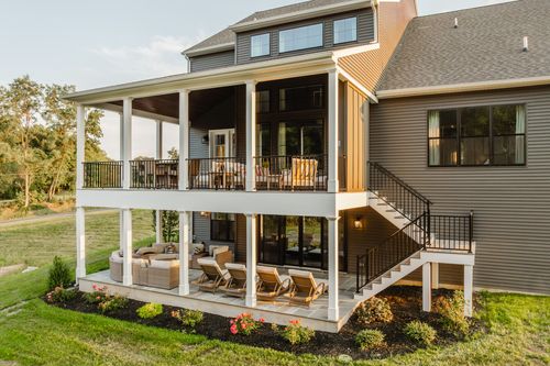 Rear porch with wicker seating, a staircase, and a stone patio overlooking open land