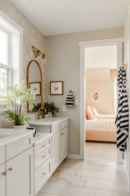 Bathroom with an arched brass mirror, scalloped tile wall and a peek into a pink bedroom