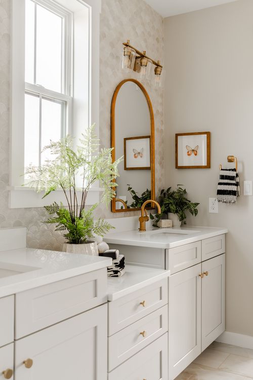 Double-sink bathroom vanity with an arched brass mirror, brass sconce and scalloped tile