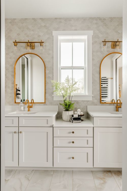 Double-sink bathroom vanity with arched brass mirrors, brass sconces and scalloped tile
