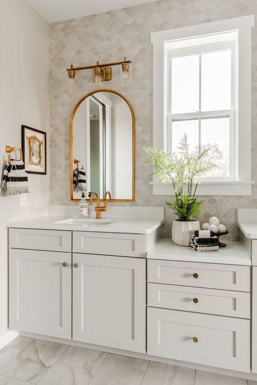 Bathroom vanity with an arched brass mirror, scalloped tile wall and brass fixtures