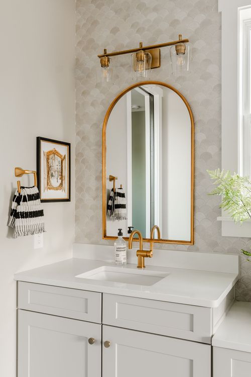 Bathroom vanity close-up with an arched brass mirror and scalloped tile backsplash