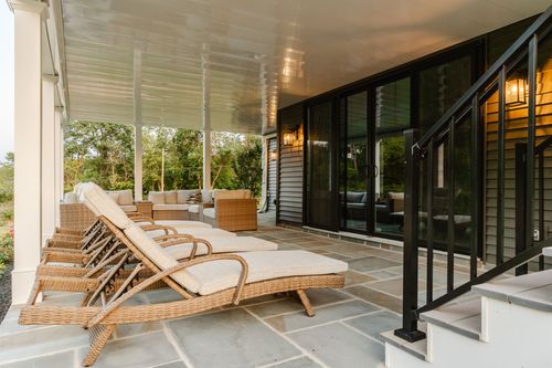 Covered stone patio with wicker chaise lounges beneath a beadboard porch ceiling