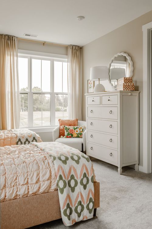 White dresser with a scalloped mirror and lamp beside twin beds with patterned bedding