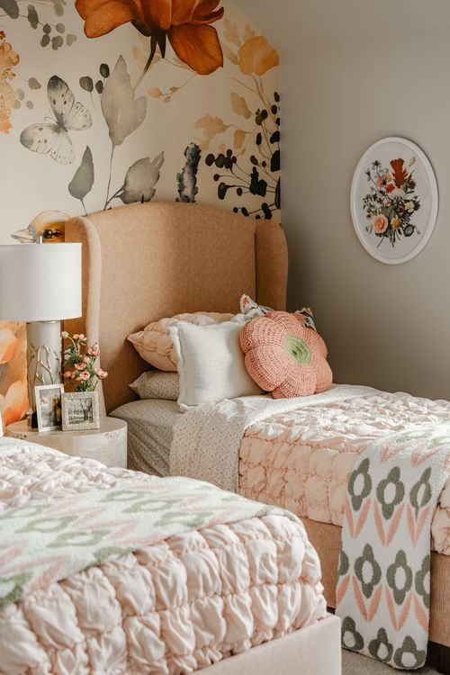Twin beds with peach upholstered headboards under a bold floral wallpaper mural