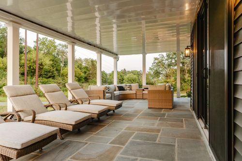Covered stone patio with wicker lounge chairs and a view of rolling green fields