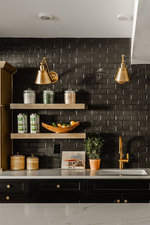 Black brick backsplash with brass sconces, open shelving and a brass gooseneck faucet