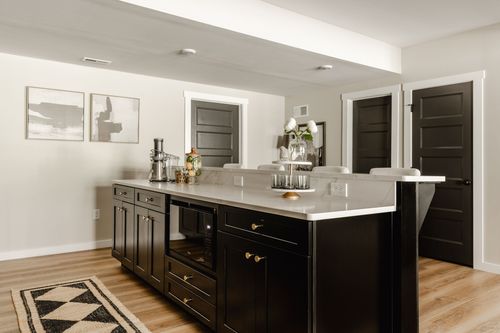 Basement bar island with black cabinetry, quartz countertop and dark doors beyond