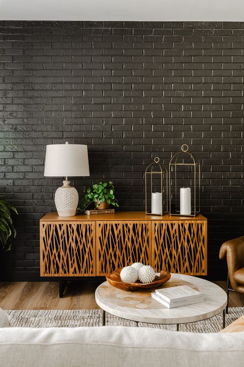 Wood woven-front media console with candle lanterns against a black brick accent wall