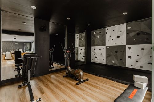 Home gym with a black climbing wall, elliptical machine and mirrored wall