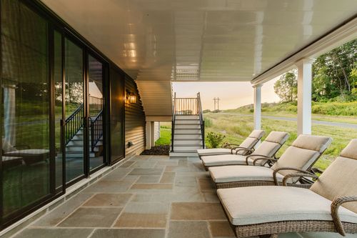 Covered stone patio with wicker chaise lounges and glass sliding doors at sunset