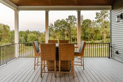 Covered wood deck with a wicker bar-height dining set overlooking open fields at dusk