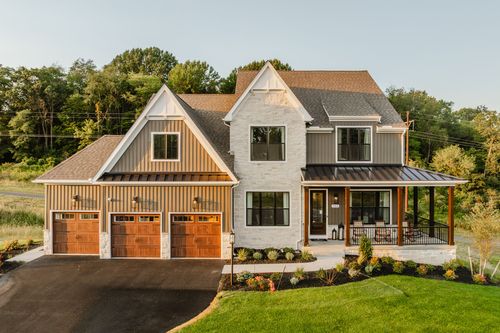 Aerial view of a modern farmhouse with stone and board-and-batten siding at golden hour