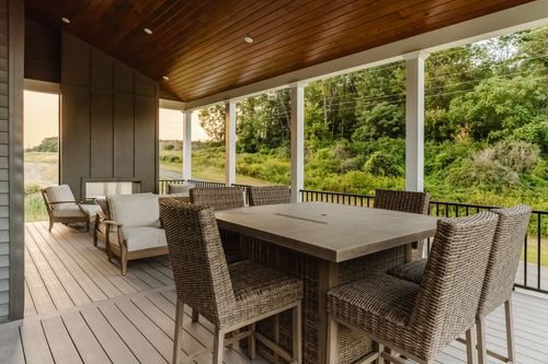 Covered porch dining area with a wicker bar-height table beside a board-and-batten accent wall