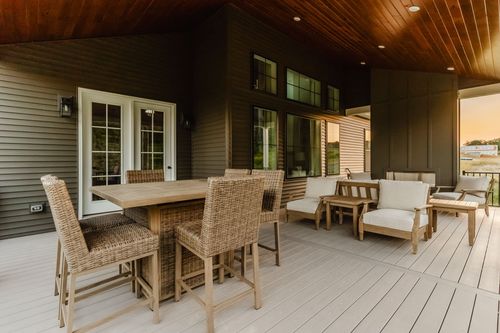 Covered porch with a wicker bar table, sectional seating, and a wood-paneled accent wall