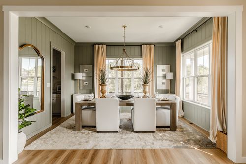 Dining room with sage green paneled walls, a brass ring chandelier, and cream upholstered chairs