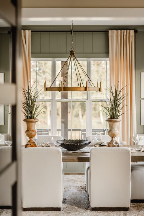 Dining table set with wine glasses beneath a brass chandelier and tall arched windows