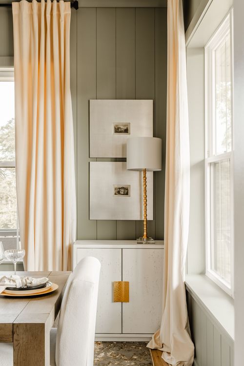 Sage green dining nook corner with a gold-hardware cabinet, table lamp, and framed art