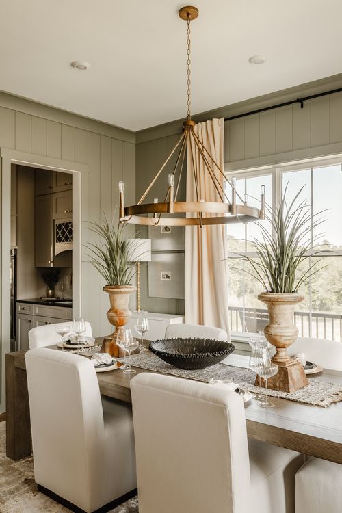 Dining room with a brass ring chandelier and sage paneled walls opening to the kitchen