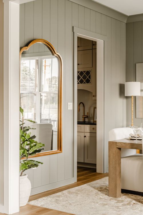 Arched gold-framed mirror reflects the kitchen through a sage green hallway