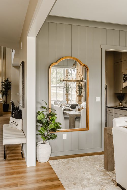 Arched brass mirror reflects the dining room chandelier from a plant-filled hallway