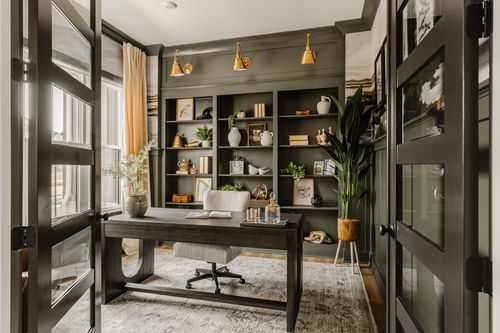 Home office with black French doors, dark green built-in bookshelves, and brass sconces