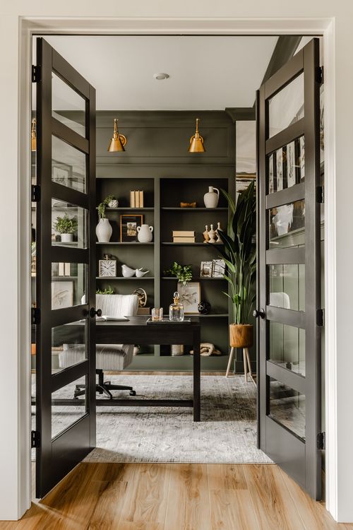 Open black French doors reveal a moody green home office with built-in shelving