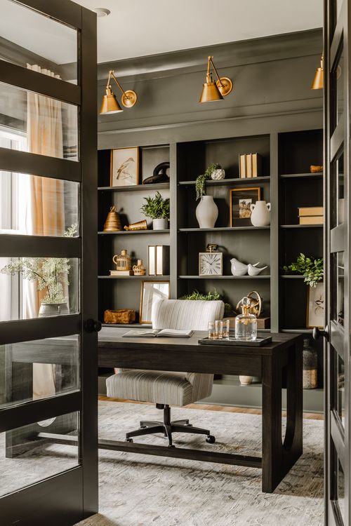 Home office with black bookshelves, brass sconce lighting, and a dark wood desk