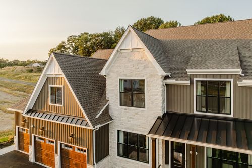 Aerial close-up of gabled rooflines, a stone chimney tower, and a three-car garage