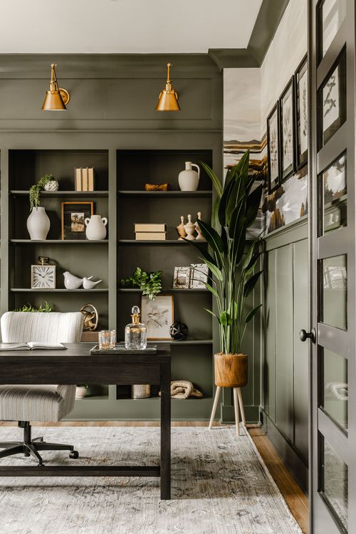 Home office with dark green built-in shelves, brass sconces, and a tall potted plant