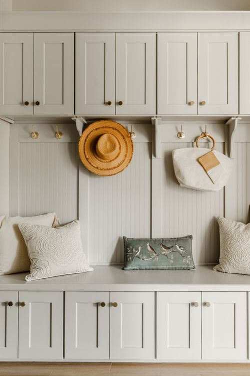 Mudroom bench detail with white cabinetry, brass hooks, and coordinating throw pillows