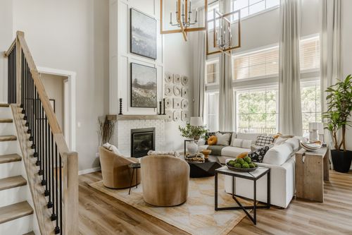 Two-story living room with a white brick fireplace, wood staircase, and neutral swivel chairs