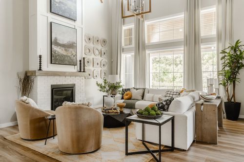 Two-story living room with a white brick fireplace, gallery wall, and curved accent chairs