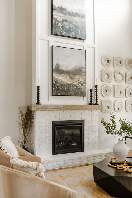 White brick fireplace detail with layered abstract art, taper candles, and a ceramic vase