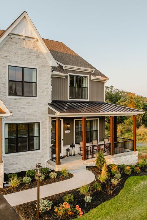 Front porch entry with a stone base, wood columns, rocking chairs, and a metal roof accent