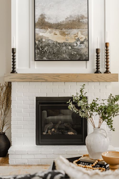 White brick fireplace mantel styled with abstract art, taper candlesticks, and a ceramic vase