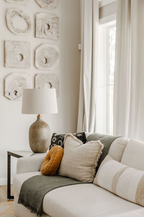 Textured ceramic-look wall art above a lamp table beside a cream sofa with layered pillows