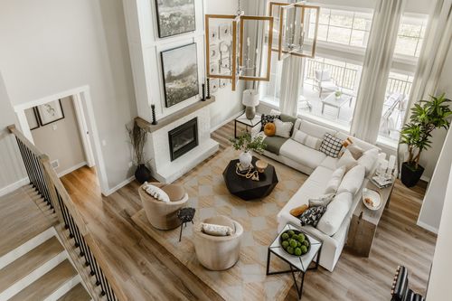 Aerial view of a great room with dual wood-framed chandeliers, fireplace, and open staircase