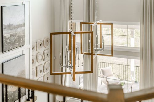 Geometric wood-framed chandeliers hang above an open stairwell landing