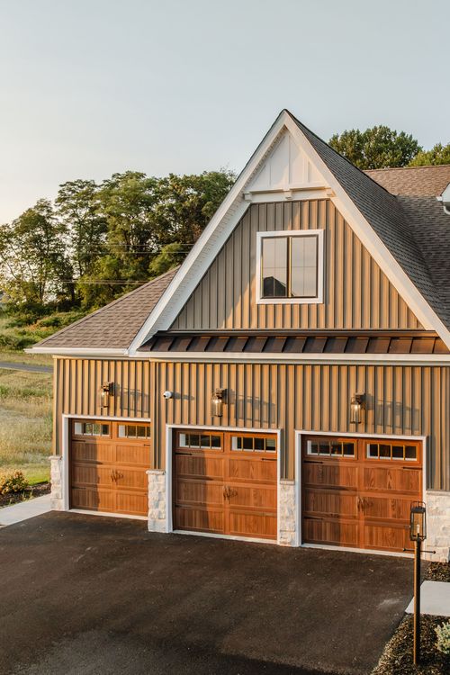 Gable end of a three-car garage with board-and-batten siding and wood-tone carriage doors