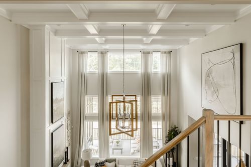 Two-story great room with a coffered ceiling, geometric chandelier, and covered balcony view