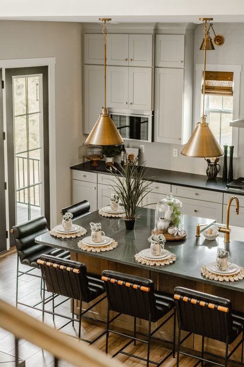 Kitchen island set for two beneath brass cone pendant lights and black countertops