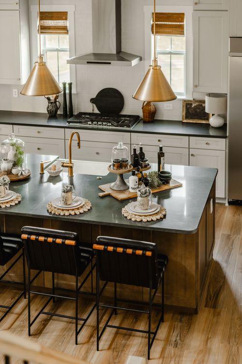 Kitchen with brass pendant lighting, black countertops, and a stainless range hood