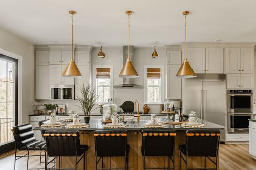 Kitchen island dining setup with brass pendants, black leather bar stools, and black countertops