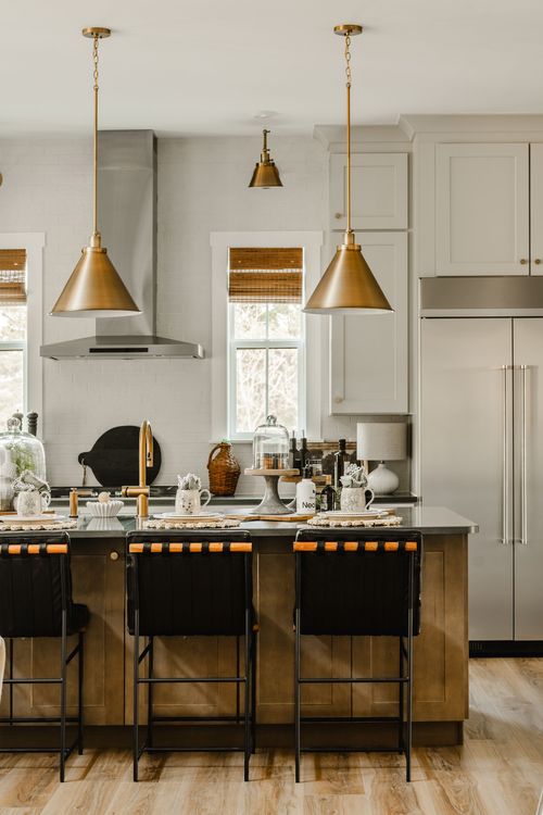 Kitchen with brass pendant lights, black leather stools, and a built-in stainless refrigerator