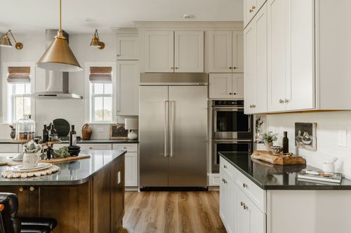 White kitchen with a stainless refrigerator, wall ovens, and black countertops