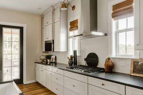 Kitchen cooktop area with a stainless range hood, black countertops, and a bay window